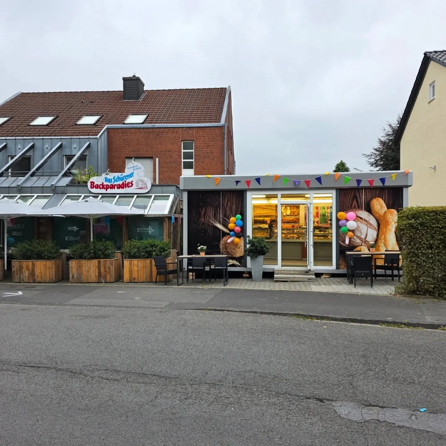 Die Ladenfront des Schürener Backparadies an der Gevelsbergstraße, mit Wimpelkette und Sitzbänken davor