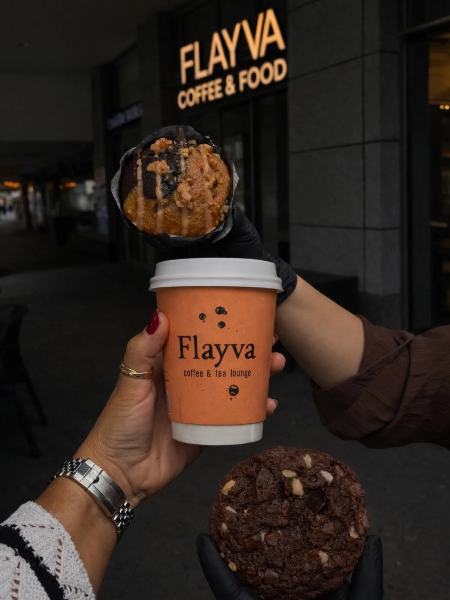 Kaffeebecher und Cookie vor dem beleuchteten Schild von Flayva Coffee & Food
