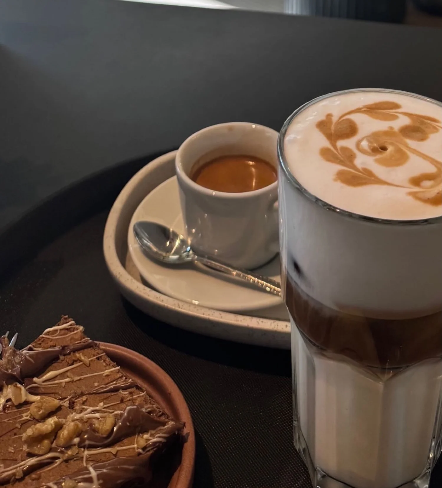 Espresso, Latte Macchiato und ein Stück Schokoladenkuchen auf dunklem Tablett